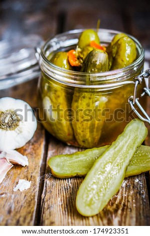 Pickles with garlic in glass jar on rustic wooden background