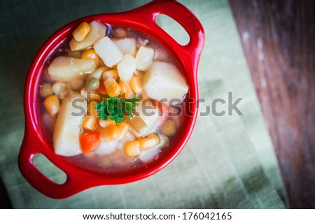 Chicken noodle soup with vegetables in red bowl on rustic table
