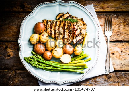 Grilled chicken with potatoes and asparagus on wooden background