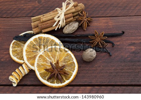 Cinnamon sticks, anise stars, nutmegs, dried orange, and vanilla beans on brown wooden background.