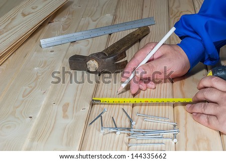 Close-up shot of hands with pencil and measure tape and wooden in background.