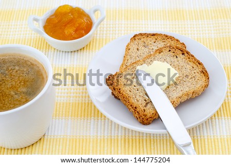 breakfast of toast with butter and jam and coffee on yellow tablecloth