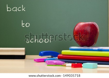 school supplies with red apple on desk green blackboard background