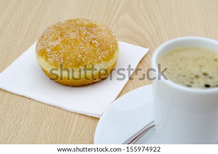 a glazed donut next to a cup of coffee in a  cup in table