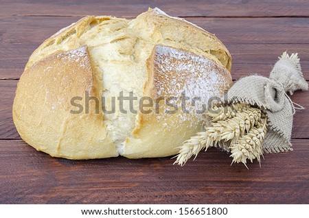 Traditional round bread with a few ears of wheat on a wooden table