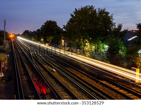 View over railway lines at twilight with the light streak of a train that has recently passed. Wimbledon, UK.
