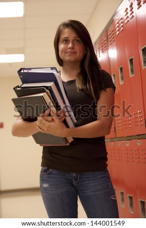 A female student poses while holding textbooks and notes by her school locker.