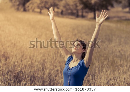 Beautiful young woman with pretty dress saying Hello to summer. Enjoying sun in nature with hands up.