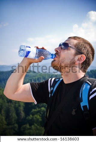 Handsome man drinking water on top of mountain