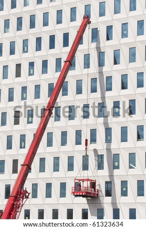 Worker wearing safety helmet and safety harness on a hoist basket hoisted by a crane