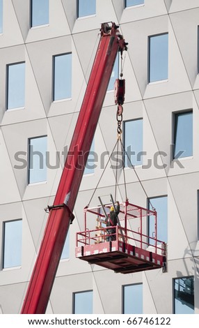 Worker in a hoisted platform  wearing safety harness gives a hand signal to the crane driver
