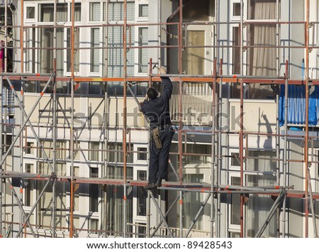 Worker wearing overall and tool belt using hammer to secure a scaffolding tube