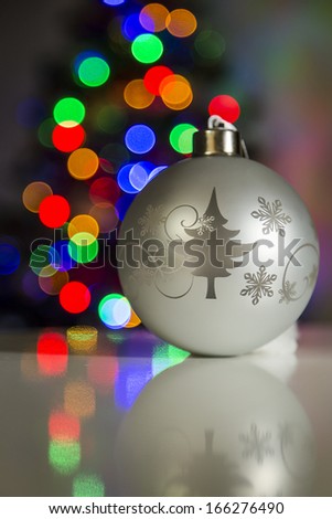 Christmas ball on a reflective table with the Christmas tree in the background