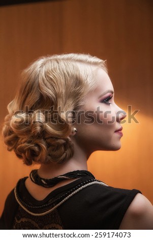 Beautiful retro chic blonde girl in black dress wearing pearls. Beauty Retro Woman Portrait. Glamour Lady. Vintage styled Girl with perfect make up and hairstyle