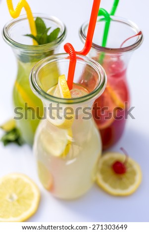 Different tips of lemonade in the jug with straws and lemons on white background. Top view