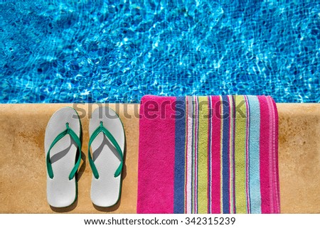 Pair of flip flop thongs and a towel on the side of a swimming pool