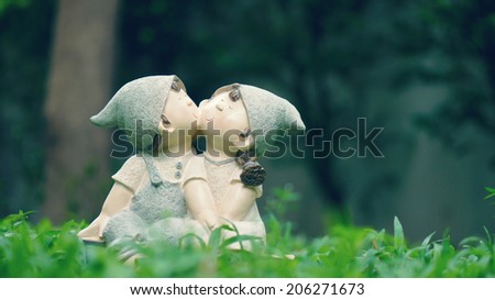 A girl and a boy dolls, kissing each other, sitting on the green grass meadow (love concept)