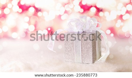 Silver gift box on white fur in pink glittering and sparkling background