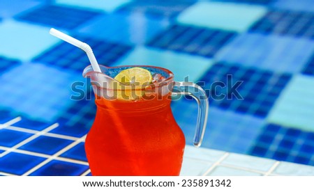 Red cold drink (lemon iced tea) with lime near swimming pool