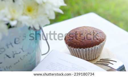 Banana cup cake with a book and flowers on white table in the garden