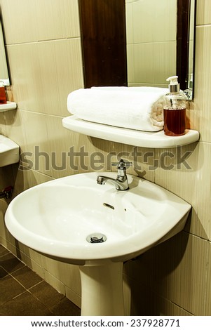 White wash basin after use and towel in the bathroom of hotel with warm white light lamp and shadows