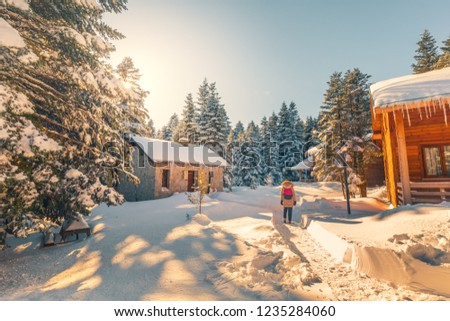 Girl walking in snowy forest meets with village houses. Snow covered trees and winter landscape. View of snow on a sunny day. Uludag National Park, Bursa, Turkey