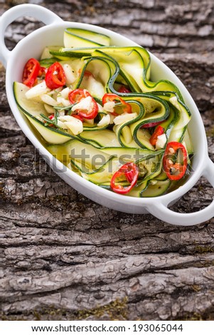 zucchini salad in white bowl on bark