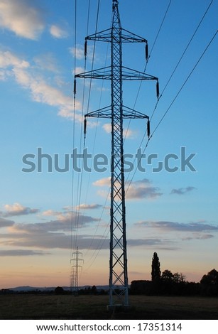 High voltage pole in front and line in diminishing perspective during evening.
