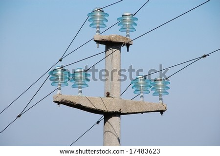 Top of a high voltage pole. The pole is made of concrete. The isolators are made of transparent glass.