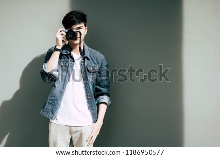 Portrait charming handsome young guy. Attractive handsome man is taking photo by using camera. Cool guy wears denim jacket, t shirt and jeans in summer season. Glamour man gets ready for vacation