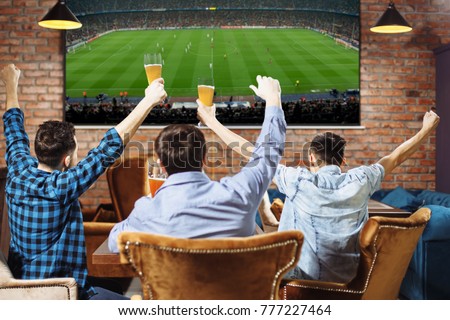 Group of young men cheering on their favorite football team watching the game on TV at the local pub having beer.