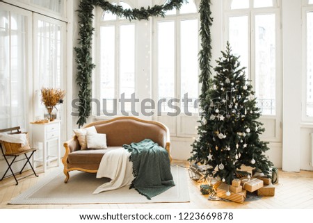 Christmas decor. Bright interior of the living room with large Windows, elegant Christmas tree with toys and garlands and a soft cozy sofa.