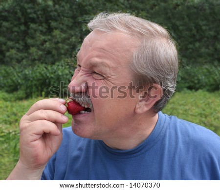 Elderly man, eating a red strawberry