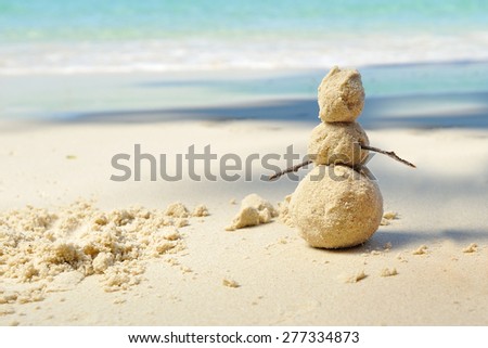 Sunny day on a tropical beach: snowman made of sand standing on the beautiful white sand coast and against on the background we can see the azure water of the sea