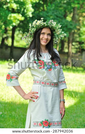 Pretty smiling young woman's portrait outdoors: she is dressed in Ukrainian national decoration - embroidered flower-ornaments on her dress and with a wreath of fresh wildflowers on her head