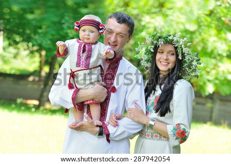 Ukrainian young and beauty family portrait outdoors: mommy and daddy and their young daughter in national dresses -  happy father is surrounded by his favorite women - wife and daughter