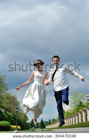 The bride and groom hold hands and jump for joy - a full-length portrait - and on a background of white, blue and purple sky before the storm