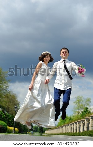 The bride and groom hold hands and jump for joy - a full-length portrait - and on a background of white, blue and purple sky before the storm