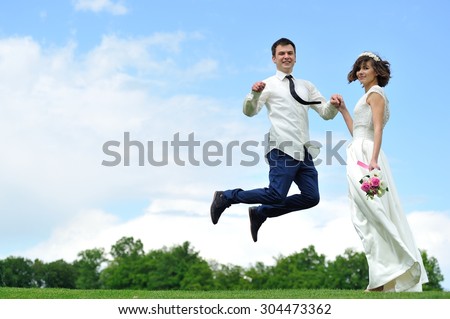 She holds his hand as he flits from happiness - a full-length portrait  of the bride and groom on a background of white and blue sky