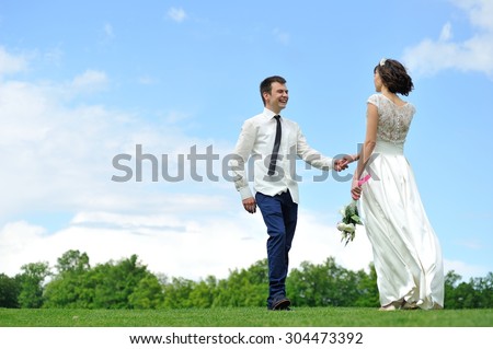 The bride inviting into the embrace his beloved bride to kiss her - under their feet is luscious green grass and over their heads - bright blue sky. They are happy