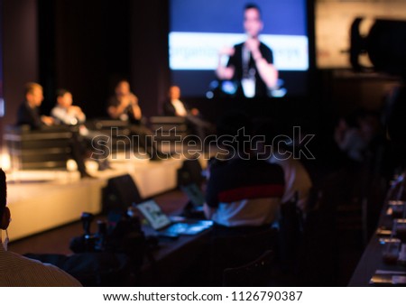 Panel Speaker on Stage Presenting Vision and Ideas. Conference Lecture Hall. Blurred De-focused Unidentifiable Presenter and Audience. People Attendees. Business Technology Event. Debate Discussion.