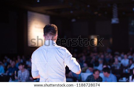 Presenter Presenting Presentation to Audience. Defocused Blurred Conference Meeting People. Lecturer on Stage. Speaker Giving Speech to Business and Technology Industry People.