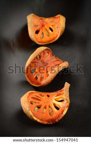 Bael paste, dried orange-yellow pieces  arranged on wooden plate black.