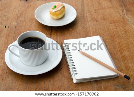 Notebook, pencil, cup of coffee and bread on the wooden floor.