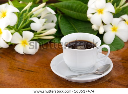 Cup of coffee on a saucer with a spoon for people to put the plate on the back with white frangipani leaves and put on the table all put a lot of wood.