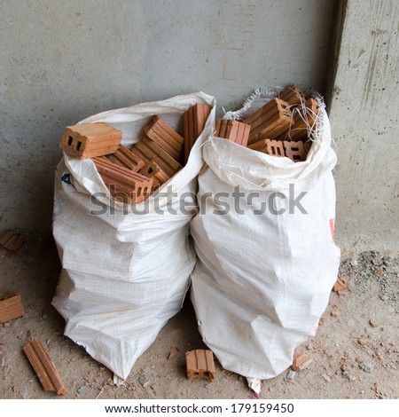 Many bricks encased in a white plastic bag on the floor and walls of concrete buildings.