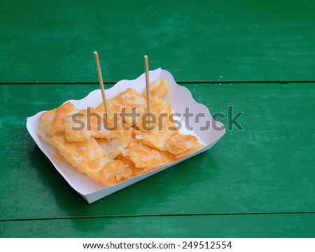 Sprinkle sugar and condensed milk, meat, fried bread, cut into pieces and placed in a white paper plate on a wooden table, painted green.