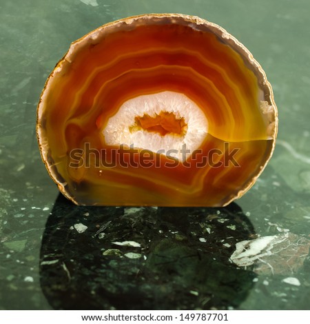 Orange agate geode on a green marble background.