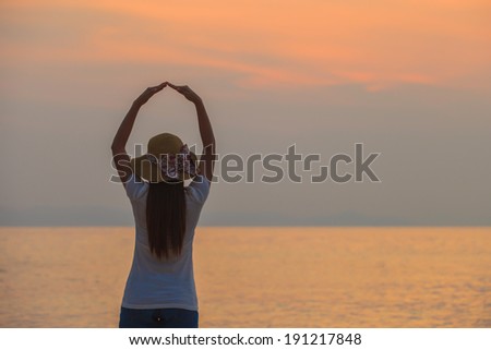 Asian woman standing in the dock after a hand-made heart shape along the sea in the evening