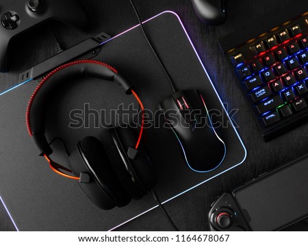 gamer workspace concept, top view a gaming gear, mouse, keyboard, joystick, headset, mobile joystick and mouse pad on black table background with RGB color.